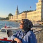 Turkish woman in hijab enjoying the scenic view by the Bosphorus in Istanbul with iconic architecture in the background.